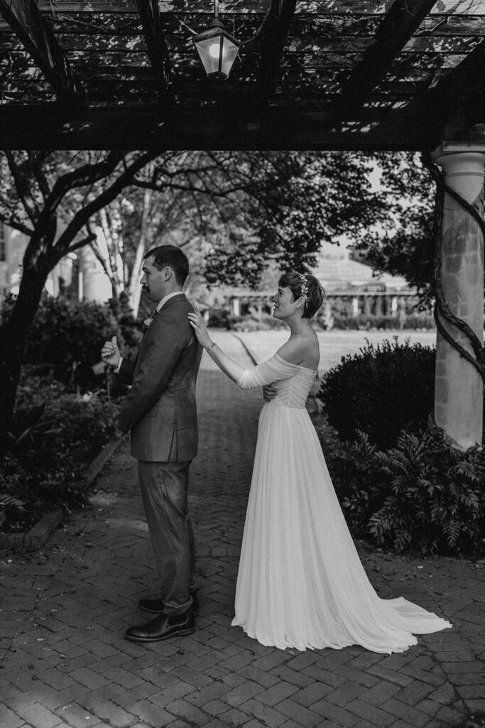  bride and groom share a quiet moment, standing close together under a pergola, with the bride gently touching the groom's shoulder.