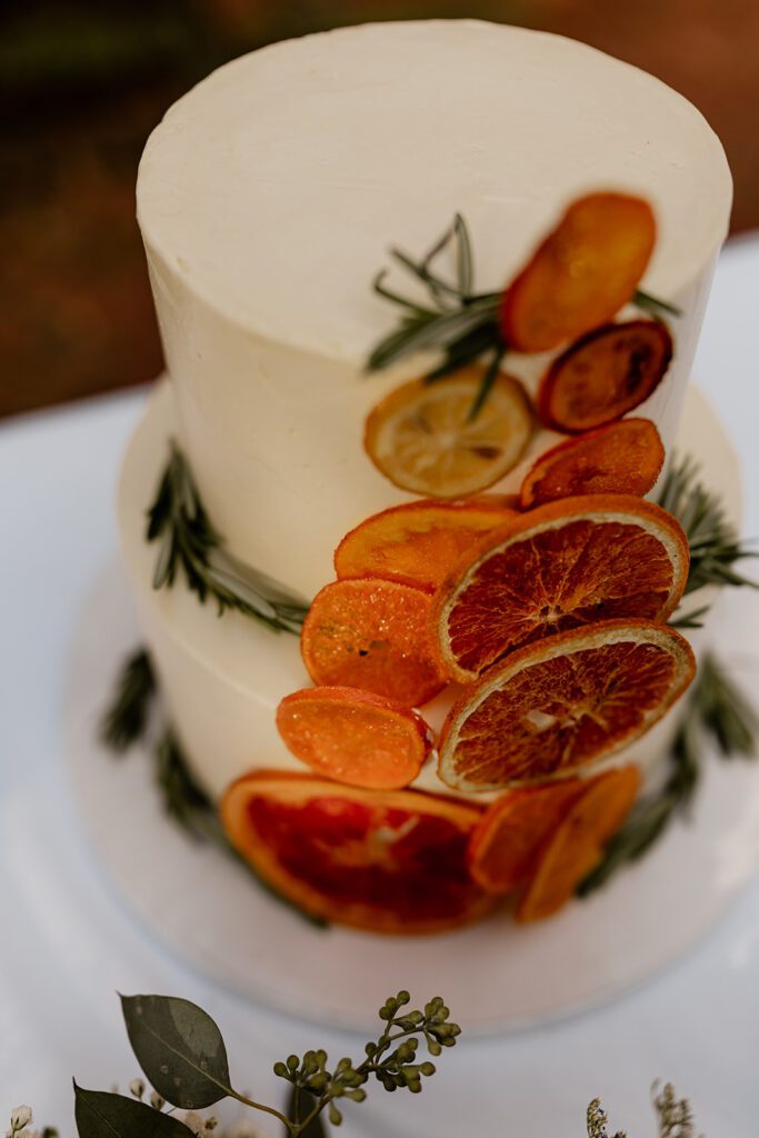 A detailed view of a two-tiered wedding cake, elegantly decorated with dried citrus slices and sprigs of rosemary.