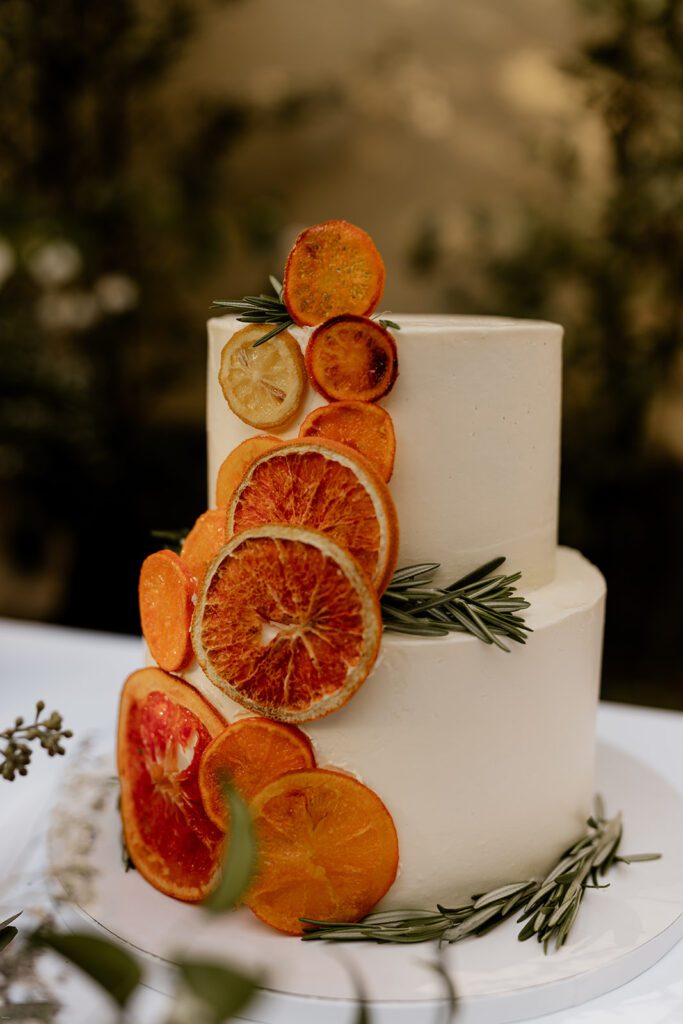 A close-up of a two-tiered wedding cake decorated with dried citrus slices and sprigs of rosemary.