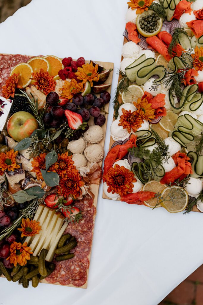 An elegantly arranged charcuterie board featuring a variety of cheeses, meats, fruits, and vegetables, decorated with vibrant flowers.