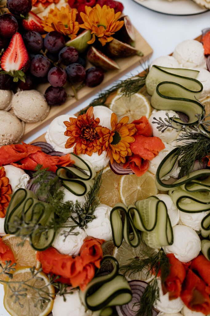 A close-up of a colorful charcuterie board showcasing a selection of fresh fruits, vegetables, cheeses, and meats, garnished with flowers and herbs.