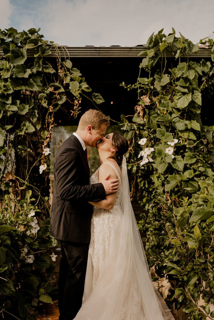 Bride and groom, Michael and Anna, sharing a kiss in front of a lush green backdrop at Hacienda Siesta Alegre in Puerto Rico.