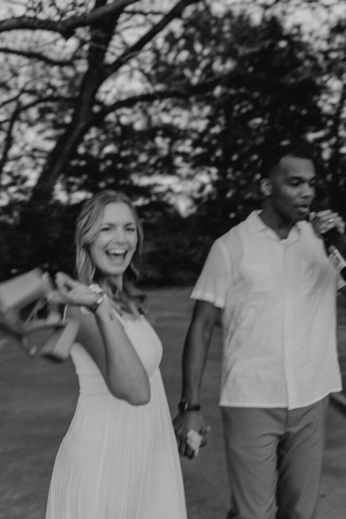 Happy couple walking hand-in-hand and smiling during their outdoor engagement photoshoot in summer attire.