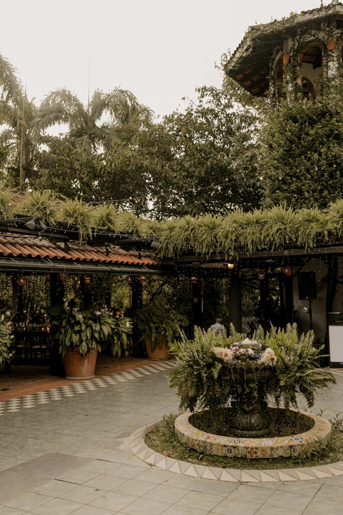 Charming courtyard at Hacienda Siesta Alegre featuring a lush, green roof, a central fountain adorned with flowers, and surrounded by greenery.