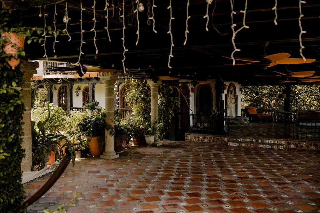 Garden Gazebo at Hacienda Siesta Alegre, featuring a tiled terrace, hanging lanterns, lush greenery, and rustic columns, creating a charming and romantic setting.