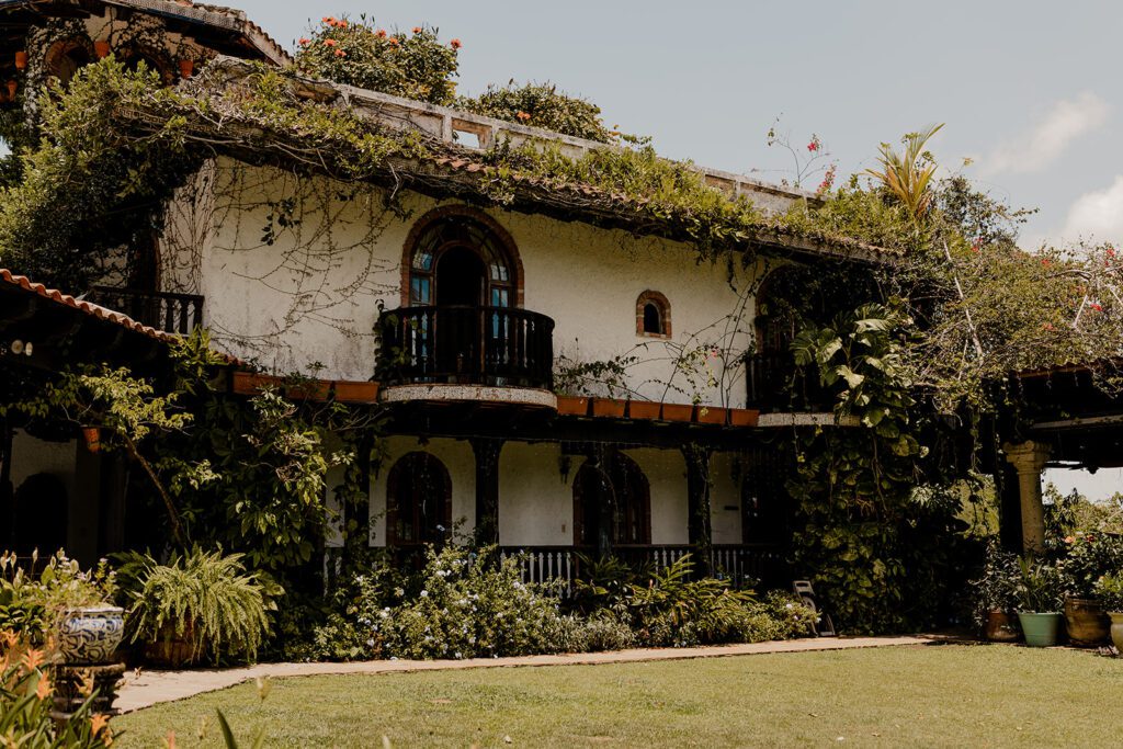 Beautifully rustic Hacienda Siesta Alegre covered in lush greenery, showcasing its classic Spanish architecture with arched doorways and a balcony