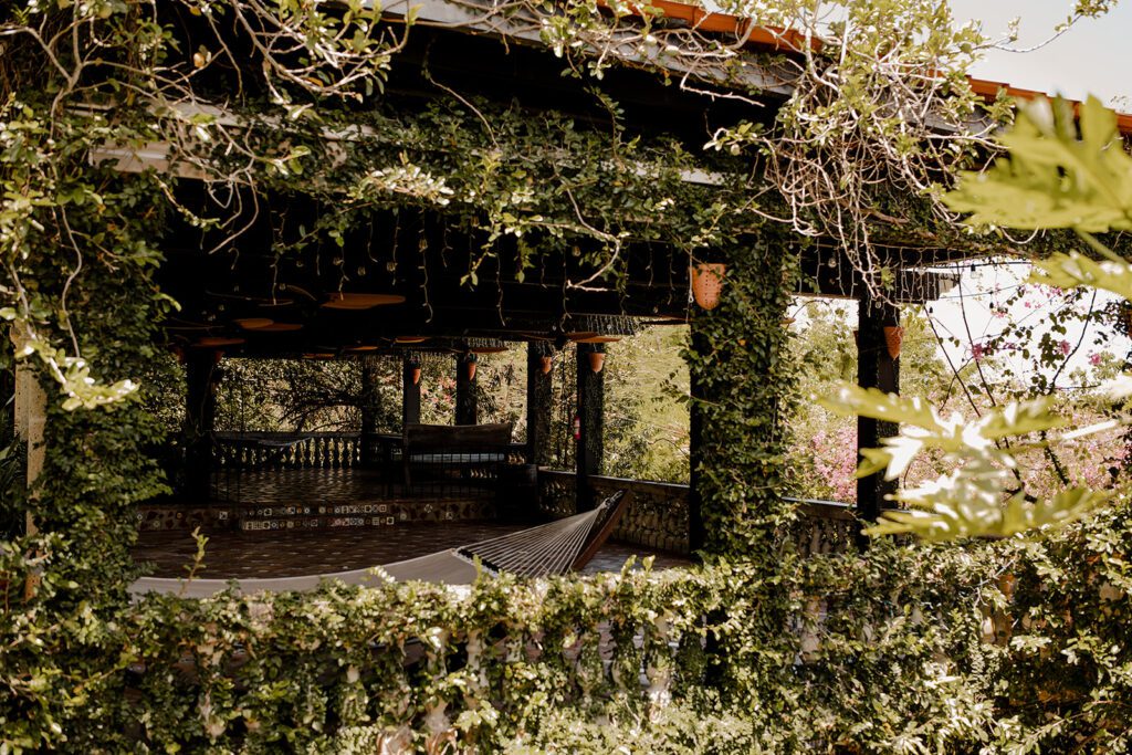 Covered outdoor seating area at Hacienda Siesta Alegre, adorned with lush vines and hanging lanterns, creating a tranquil and inviting atmosphere.