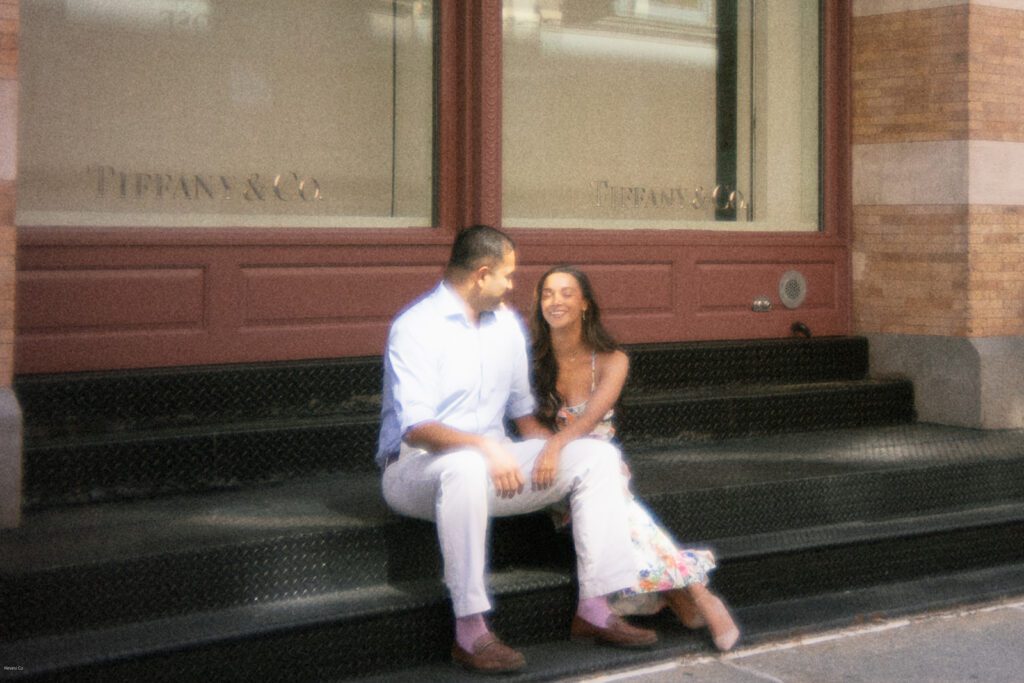 Engaged couple sitting on cast-iron steps in SoHo NYC outside Tiffany & Co. during their editorial-style engagement session
