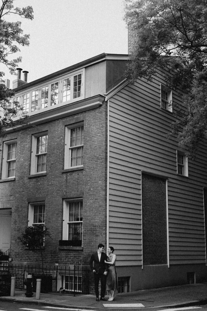 Engaged couple walking in front of a historic brick and wood-paneled townhouse in West Village NYC

