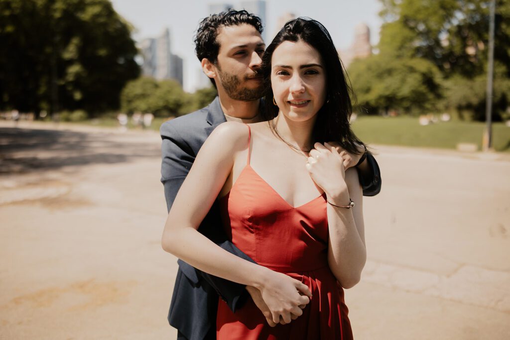 Engaged couple embracing in Central Park NYC with skyline in the background during a classic summer engagement session

