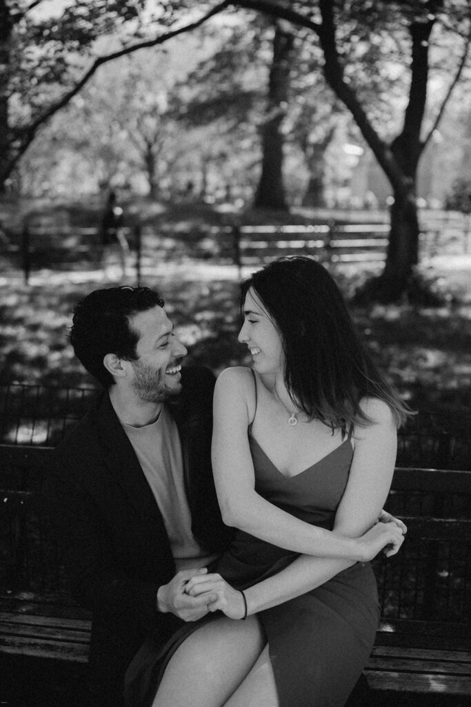 Black-and-white close-up of engaged couple laughing together on a Central Park bench

