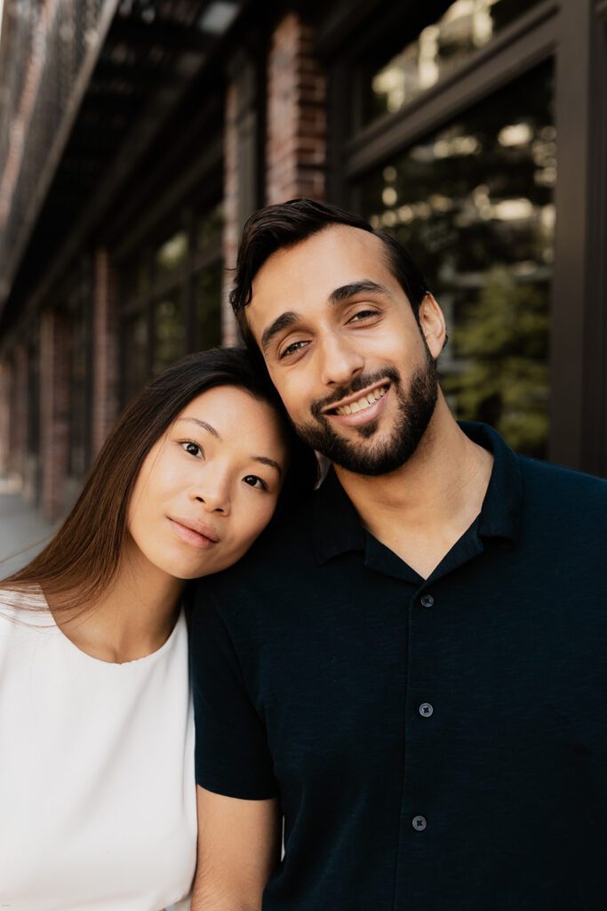 Engaged couple standing outside Chelsea storefront, woman resting her head on fiancé's shoulder

