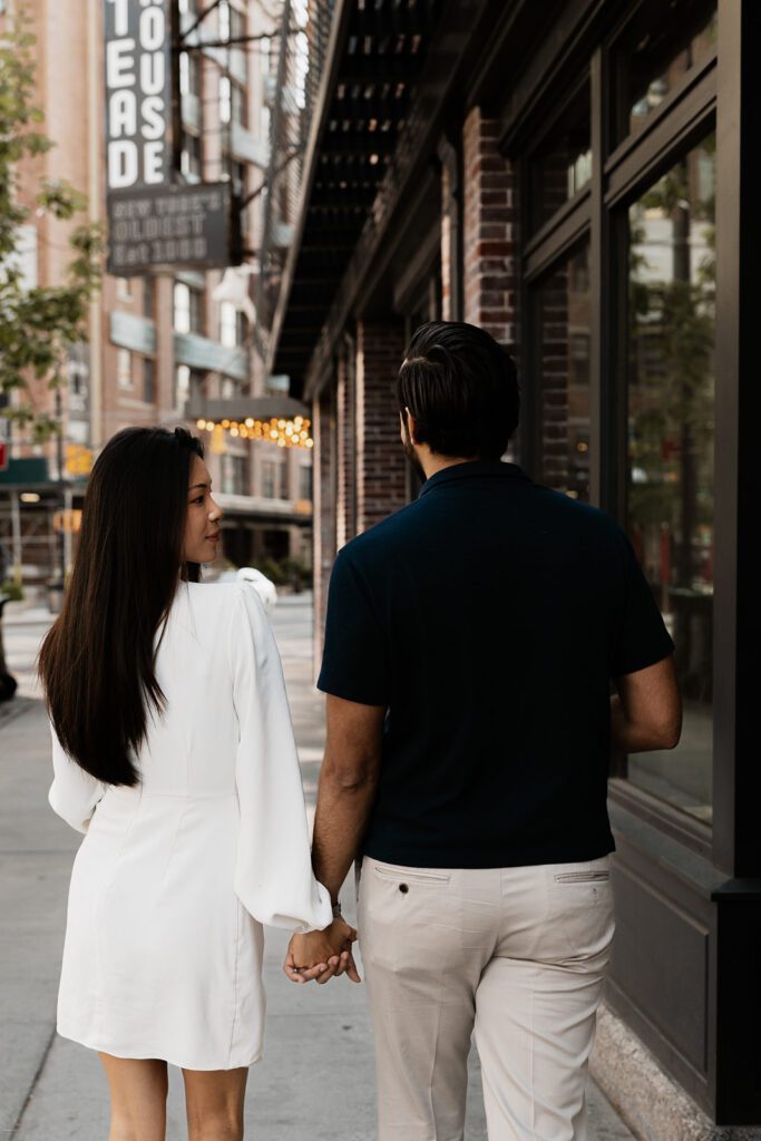Couple walking hand-in-hand past a brick building in Chelsea during their engagement session

