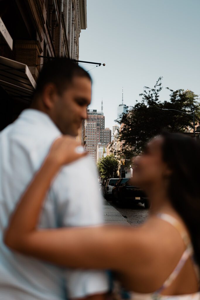 Engaged couple with SoHo skyline in the background, shot with artistic foreground blur

