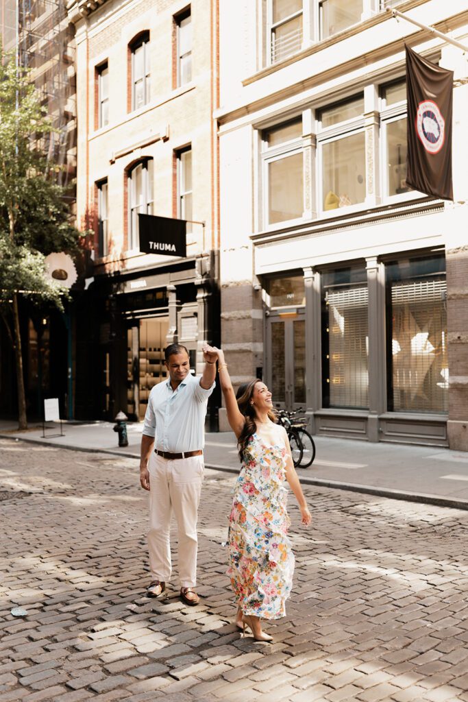 Engaged couple dancing on cobblestone street in SoHo NYC during golden hour engagement session


