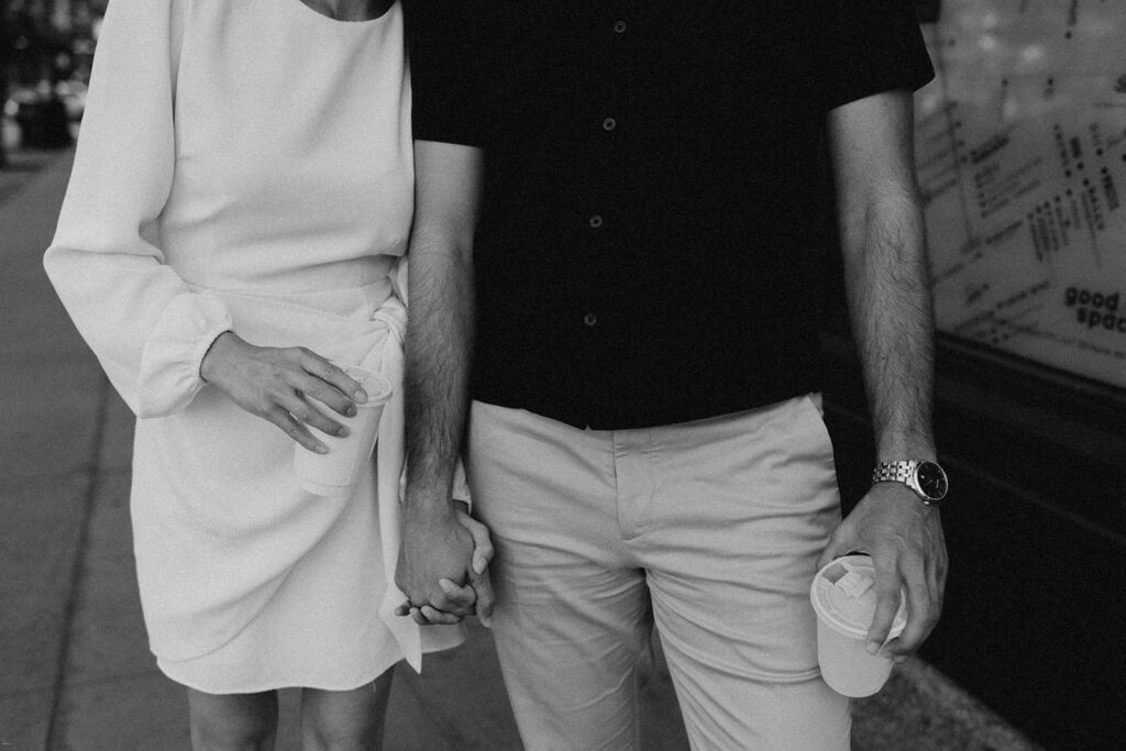 Black-and-white close-up of engaged couple holding hands with coffee cups during their Chelsea NYC engagement session

