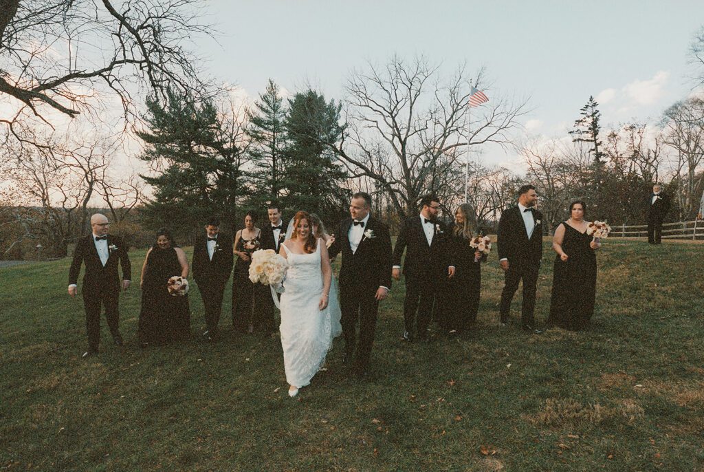 Bridal party walking together across the lawn, with the bride and groom smiling in the center on an autumn afternoon.nexy
