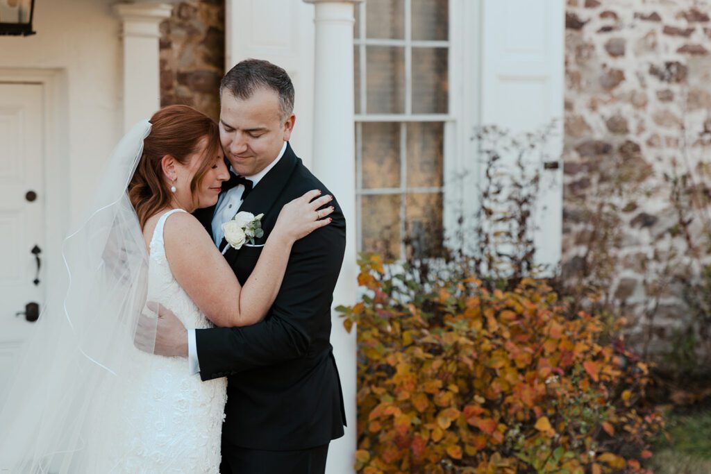 Groom hugging a family member in front of the stone house at the John James Audubon Center during a candid moment before the ceremony.