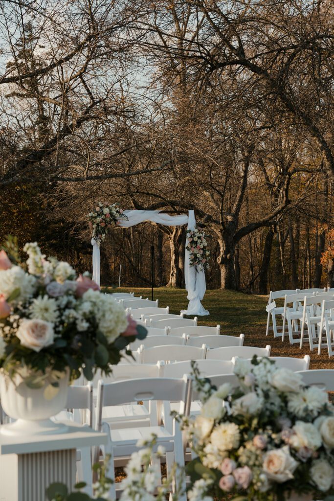 Ceremony arbor adorned with florals and white chairs set up in the apple orchard at the John James Audubon Center.